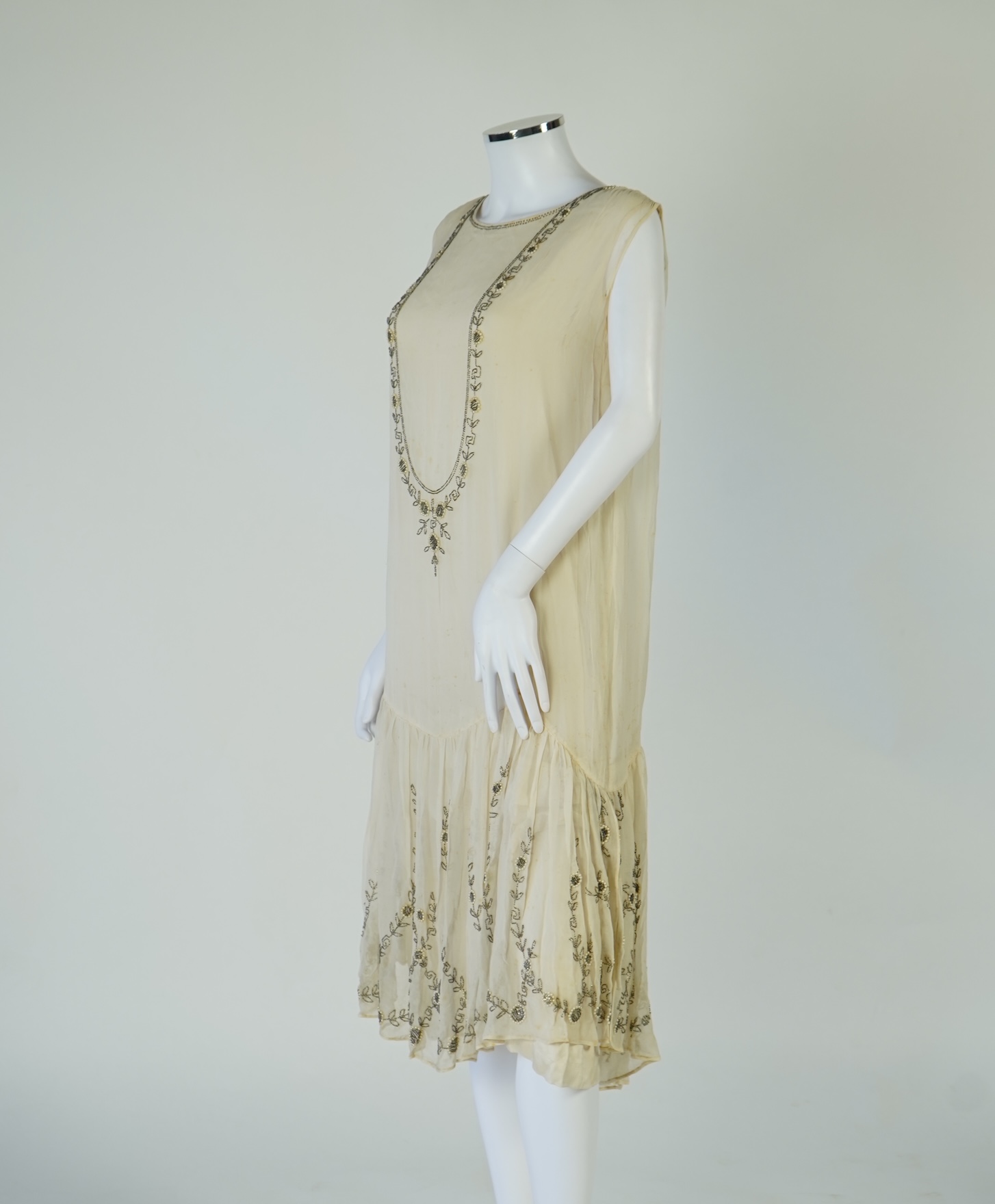 A 1920's cream silk georgette three quarter length, silk lined ‘flapper dress’. Designed with beaded and pearl floral embroidery, a stylish long beaded keyhole slit at the back, a beaded front bodice and flying beaded pa